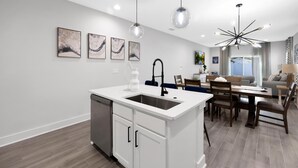 Une cuisine moderne avec des meubles blancs, un îlot central doté d’un évier et des luminaires suspendus.