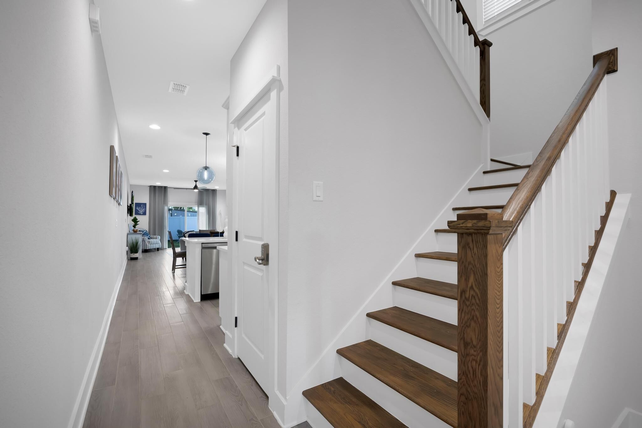 A modern interior with a wooden staircase, white walls, and a kitchen area visible in the background.