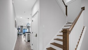 Un intérieur moderne avec un escalier en bois, des murs blancs et un espace cuisine visible au fond.