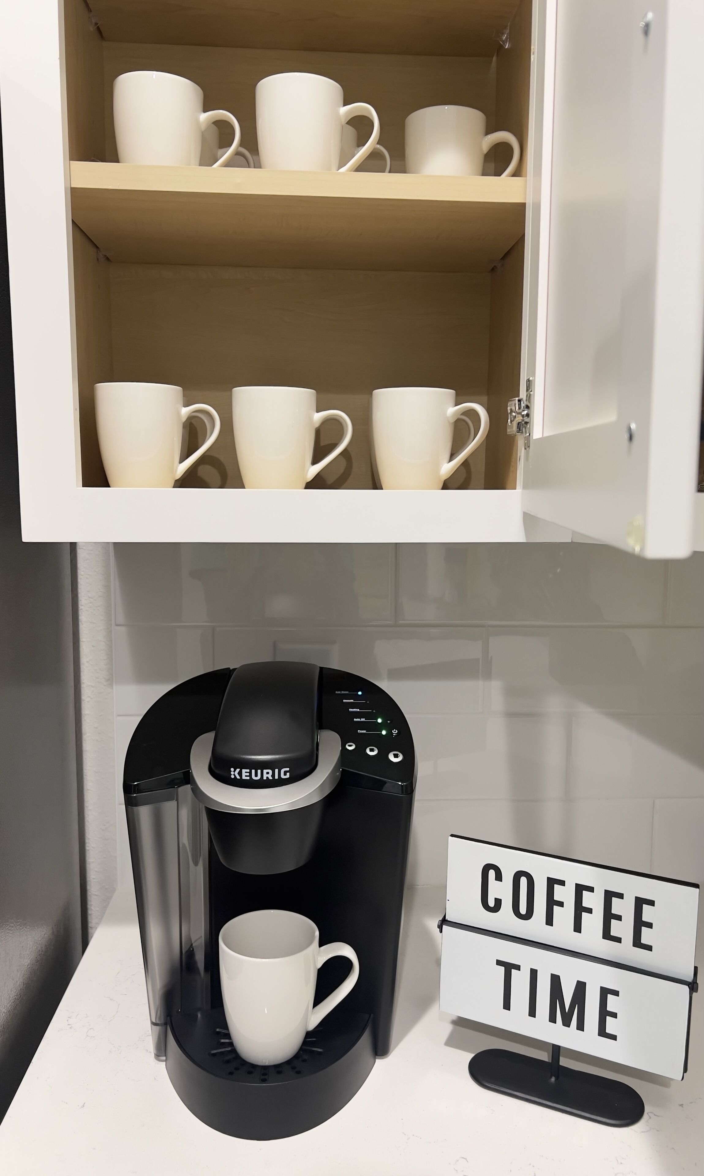 Une machine à café avec une tasse en dessous et une pancarte indiquant « C’EST L’HEURE DU CAFÉ ».