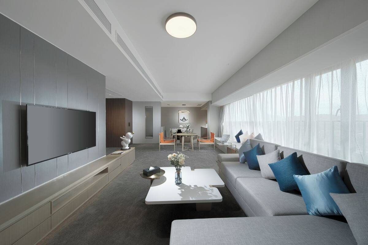 Un salon moderne avec un téléviseur à écran plat, un canapé, une table basse et un coin repas à l’arrière-plan.