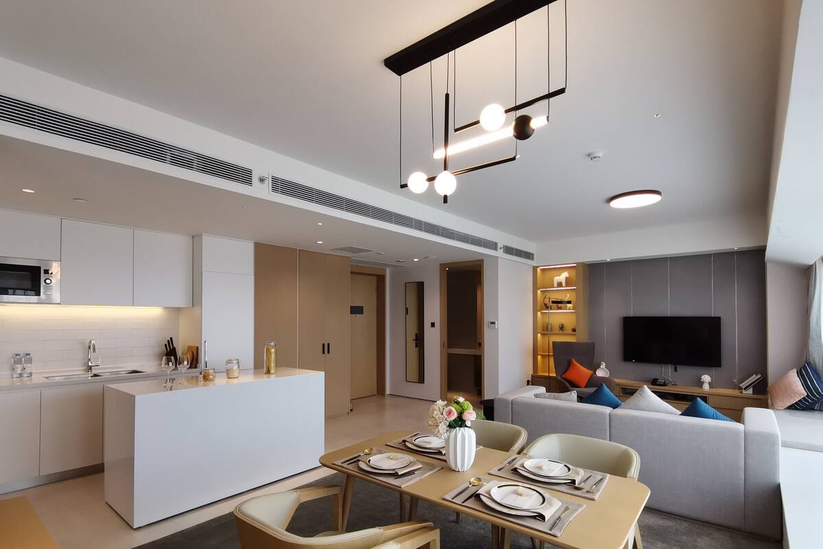 Une cuisine moderne avec des meubles blancs, un îlot central et un coin repas avec une table dressée pour quatre personnes.