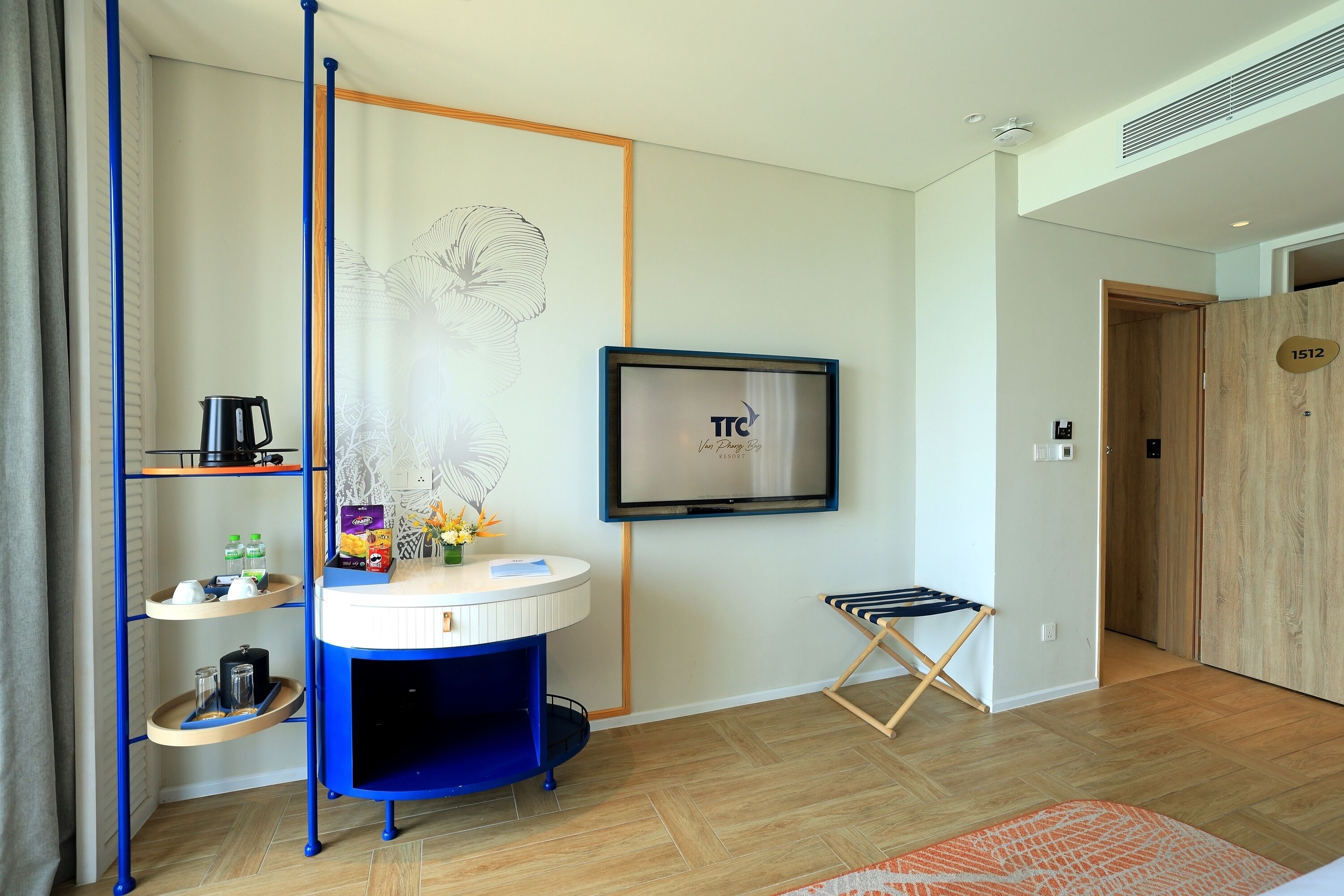 A modern hotel room with a blue and white minibar, a flat-screen TV, and a wooden door with the number 1512.