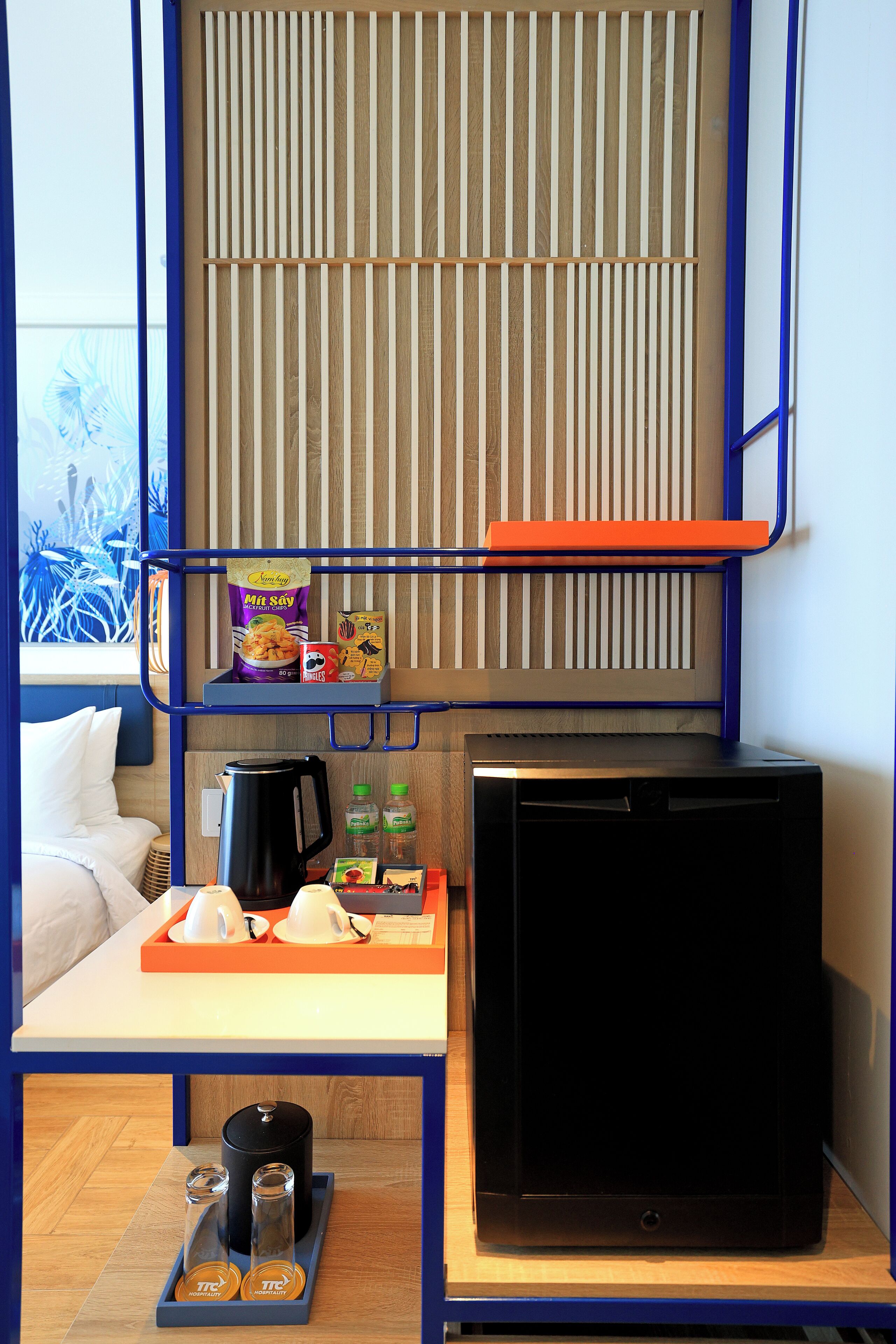 A compact room with a bed, a coffee table, a refrigerator, and a shelf with snacks.