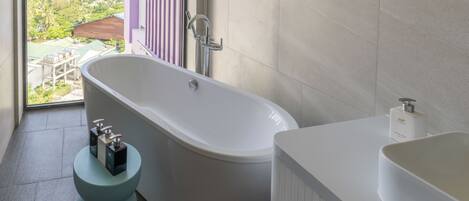 Une salle de bain moderne avec une baignoire sur pieds, un lavabo blanc et une vue sur un paysage tropical grâce à une grande fenêtre.
