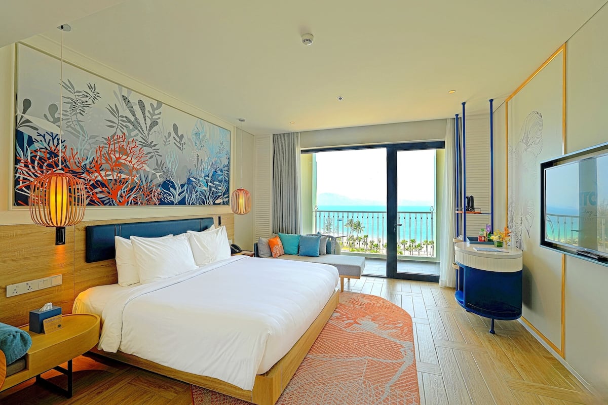 A modern hotel room with a large bed, a balcony with a view, and a TV.