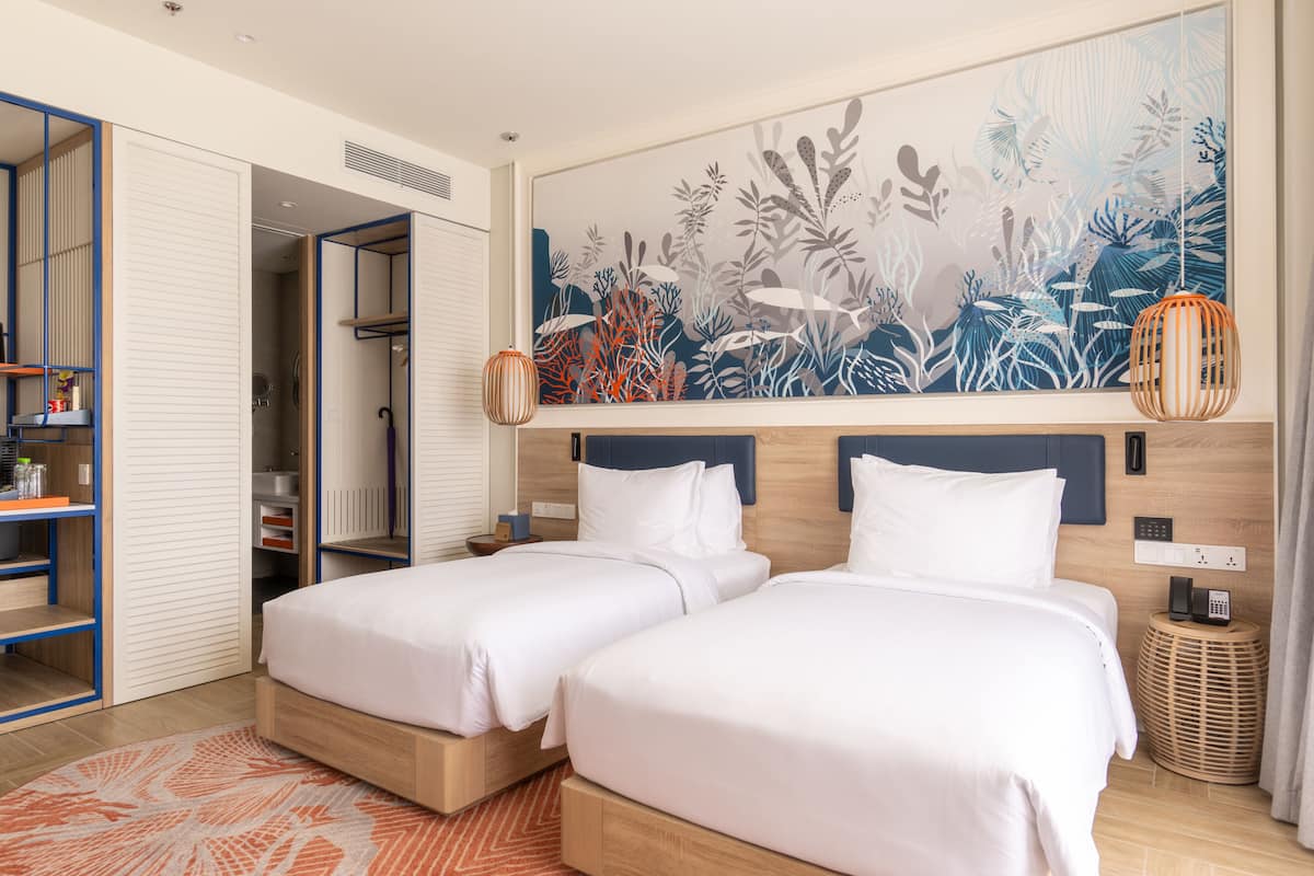 A hotel room with two beds, a wardrobe, a bathroom, and a large wall mural.