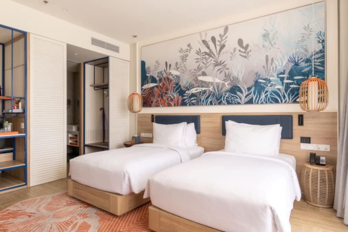 A hotel room with two beds, a large wall mural, a wardrobe, and a small side table.