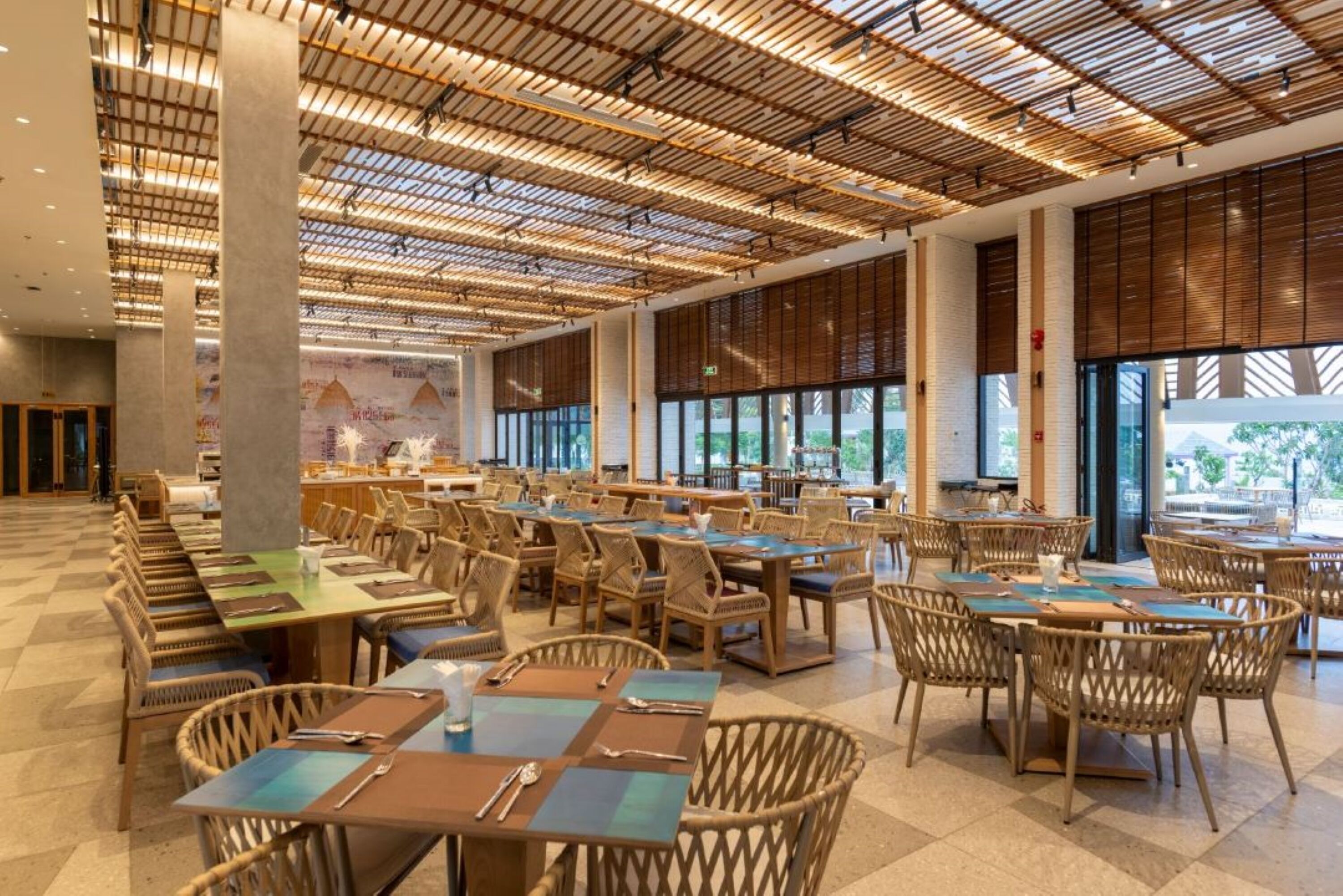 A spacious dining area with high ceilings and large windows, featuring multiple tables and chairs.