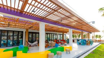 Relax in a vibrant outdoor lounge with curved seating and casual dining areas under a shaded pergola.