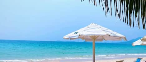 Een privéstrand, wit zand, ligstoelen aan het strand, parasols