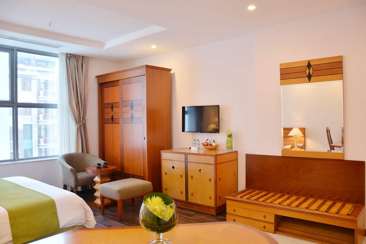 Quarto de hotel com cama, secretária, cadeira, guarda-roupa, televisão e espelho.