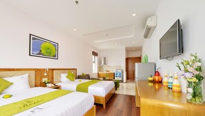 A hotel room with two beds, a wooden headboard, a flat-screen TV, a desk with a vase of flowers, and a kitchen area in the background. - Richico Luxury Apartel Ocean (Da Nang)