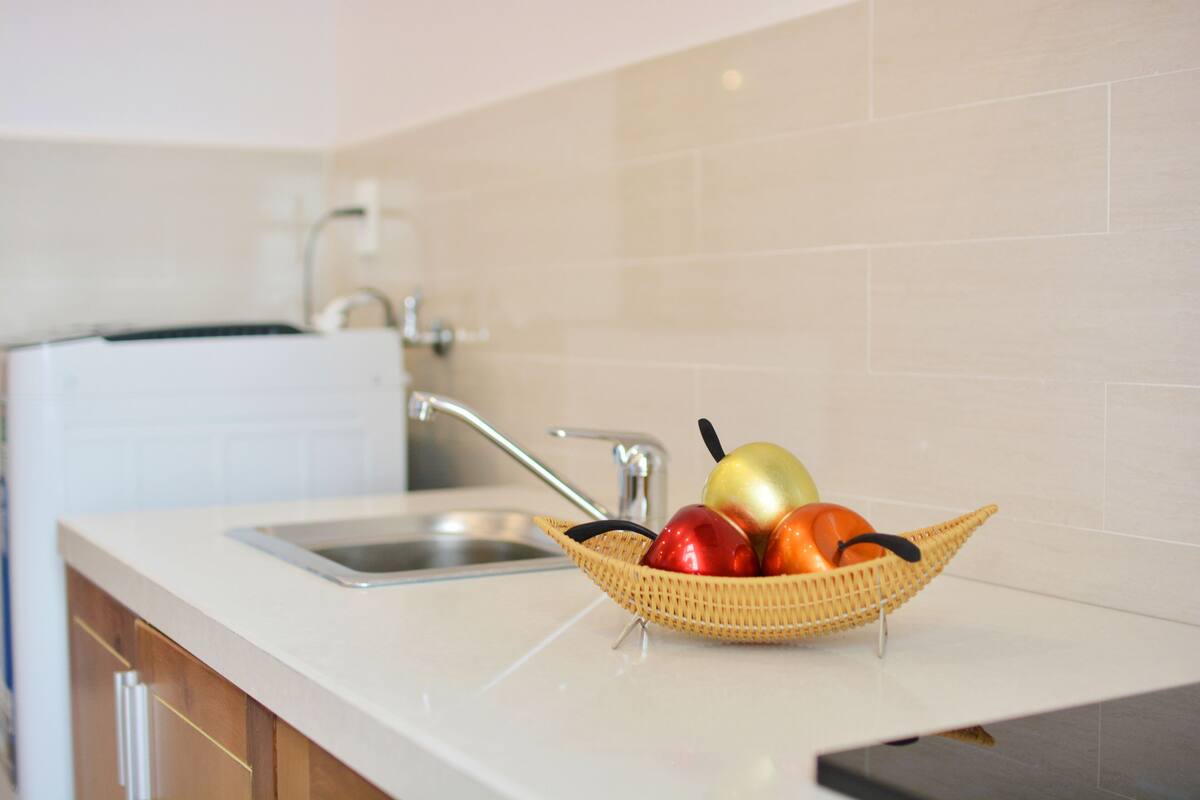 Uma bancada de cozinha com uma cesta de frutas contendo maçãs e laranjas.