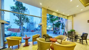 A modern hotel lobby with yellow armchairs, a dining area, and large windows offering a view of the street. - Richico Luxury Apartel Ocean (Da Nang)
