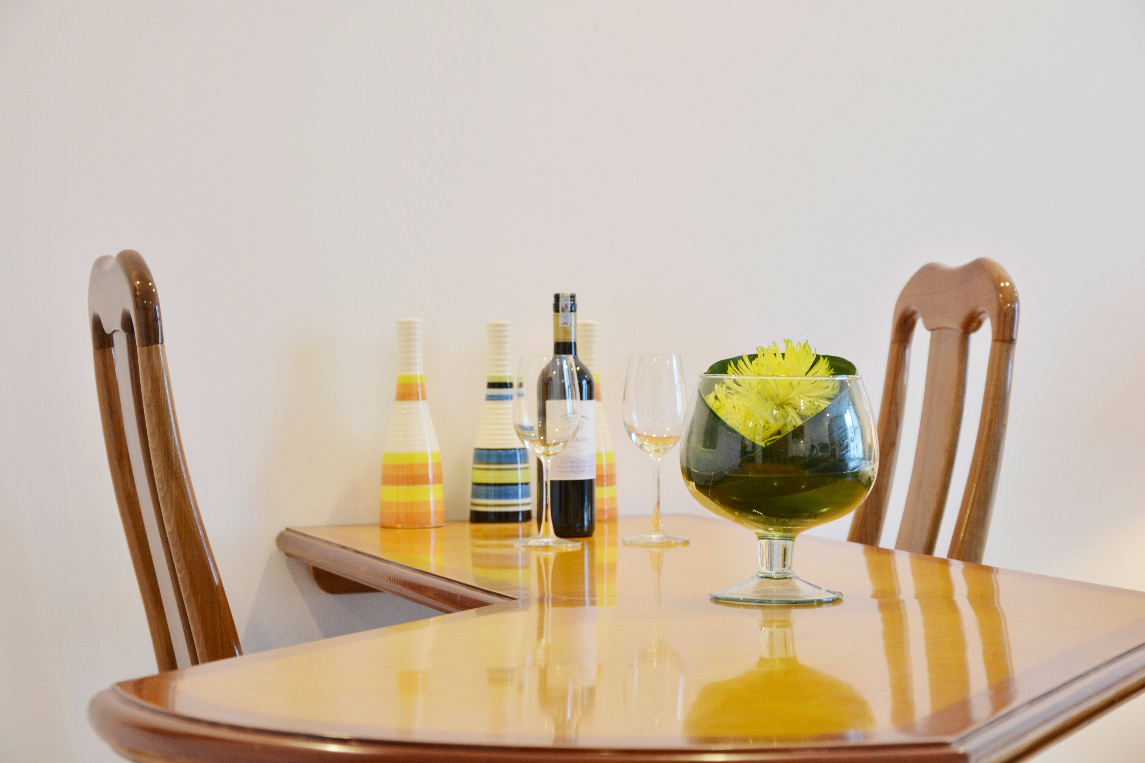 A dining table with a glass bowl containing a green garnish, two wine bottles, and two wine glasses.