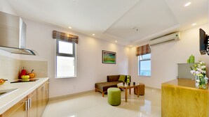 A modern kitchen with a dining area, a sofa, and a small table. - Richico Luxury Apartel Ocean (Da Nang)
