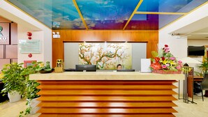 A hotel reception desk with a modern design, featuring a wooden counter, a digital screen, and a large abstract mural on the wall. - Richico Luxury Apartel Ocean (Da Nang)