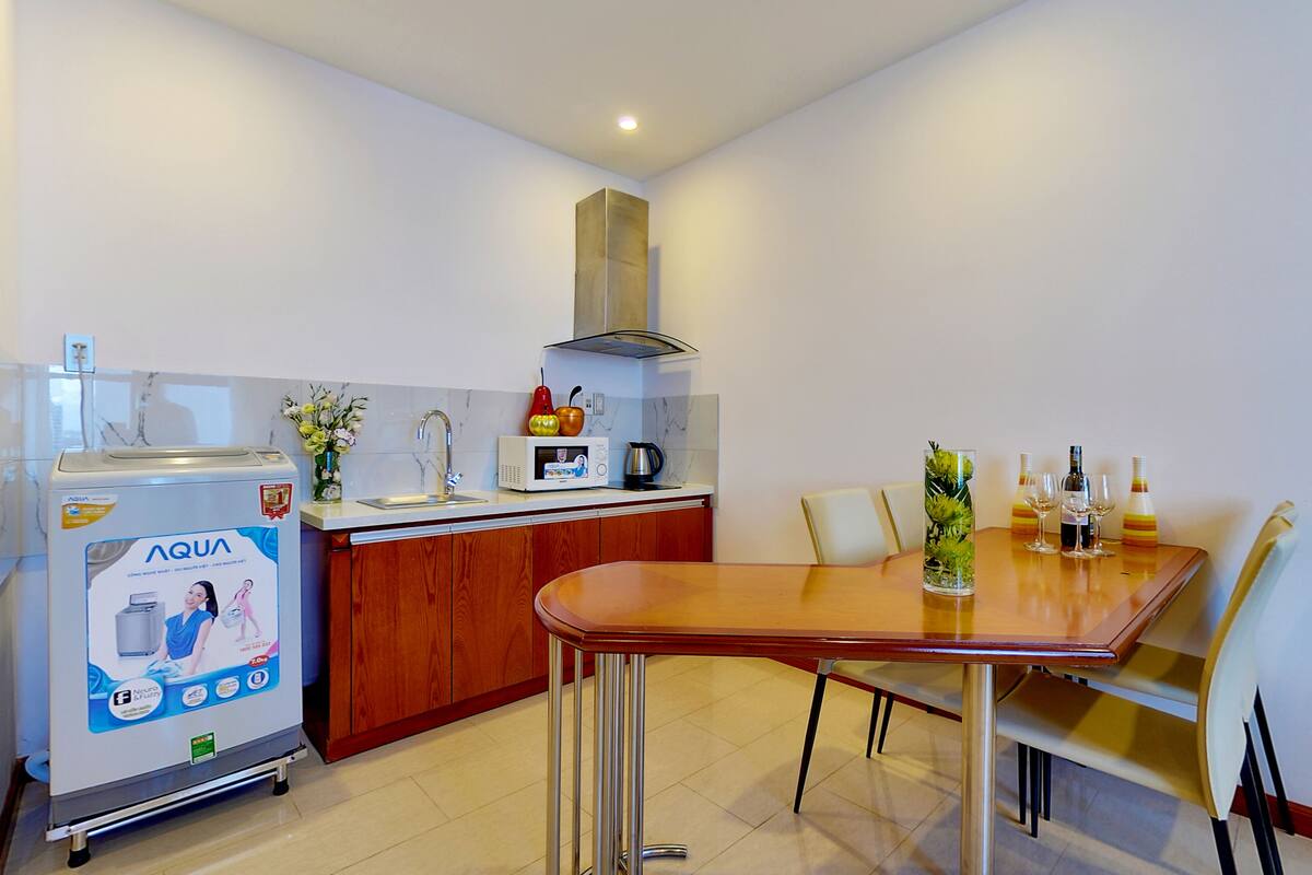 Cozinha compacta com geladeira, micro-ondas e pia. Há uma mesa de jantar com cadeiras e um vaso com flores.