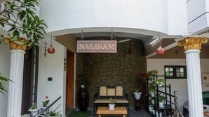 A hotel entrance with a sign reading "NALINAM HOME STAY," a stone facade, a wooden bench, and potted plants. - "NALINAM HOME STAY"  with Bed & Breakfast , Near to Sri Padmanabha Swamy Temple. (Thiruvananthapuram)