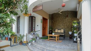 A hotel entrance with a stone wall, a wooden bench, and potted plants. - "NALINAM HOME STAY"  with Bed & Breakfast , Near to Sri Padmanabha Swamy Temple. (Thiruvananthapuram)