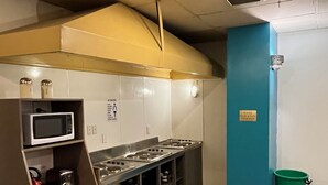 Cocina compacta con microondas, tostadora y estufa. Hay un cubo de basura y un cartel en la pared.