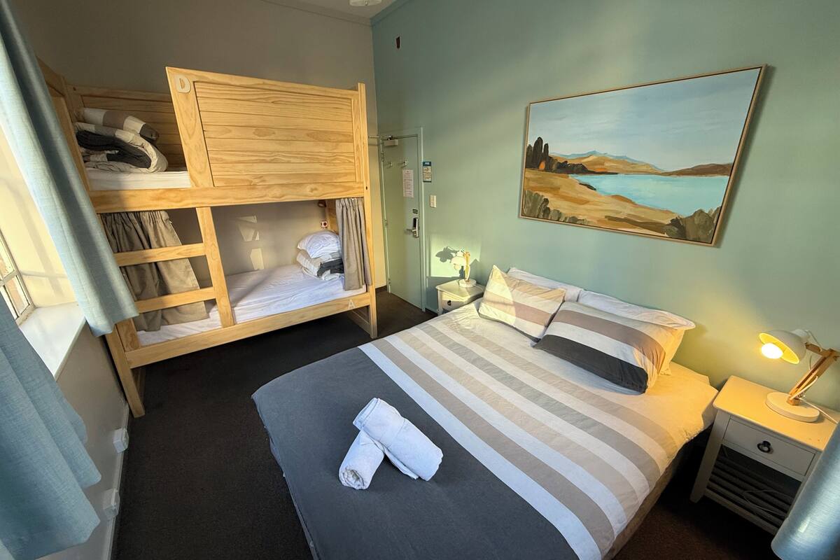 Une chambre avec un lit superposé, un lit simple, un tableau, une table de chevet et une lampe.