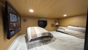 Un dormitorio con techo de madera, un televisor montado mostrando 'Risers +', un espejo redondo y una repisa con una lámpara.