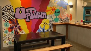 Interior de restaurante con un mural colorido, una mesa de madera y un banco.