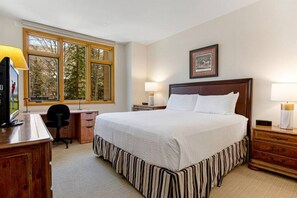 A bedroom with a large bed, a desk, a chair, a TV, and a window with a view of trees. - Highlands Lodge Beaver Creek - Corner Unit (Beaver Creek)