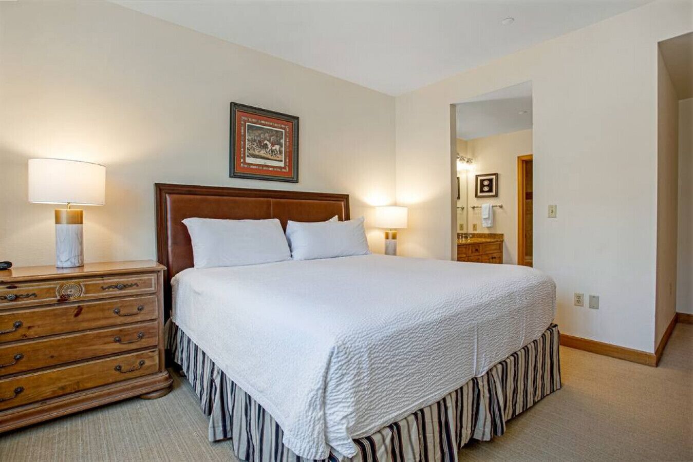 Une chambre bien rangée, avec un grand lit, une commode en bois et un tableau encadré accroché au mur.