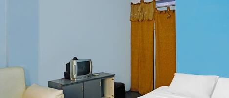 A hotel room with a bed, a chair, a desk with a television, and a wardrobe.