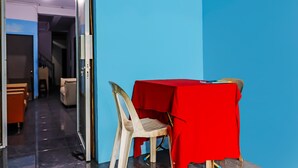 A room with a table covered by a red cloth, a plastic chair, and a door leading to another area.
