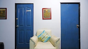 A room with two blue doors, a white chair with a pillow, and two framed pictures on the wall.