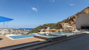 Un espace piscine comprenant plusieurs piscines, un parasol bleu et une vue sur la côte.