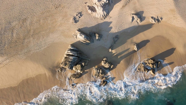 Vue aérienne d’une plage avec de grandes formations rocheuses et des vagues qui déferlent sur le rivage.