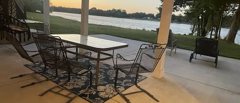 Eine Außenpatio mit Tisch und Stühlen, Blick auf ein Gewässer und einem überdachten Bereich mit Säulen.