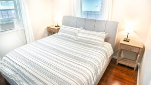 A neatly made bed with a striped bedspread, two bedside tables with lamps, and a window with blinds.