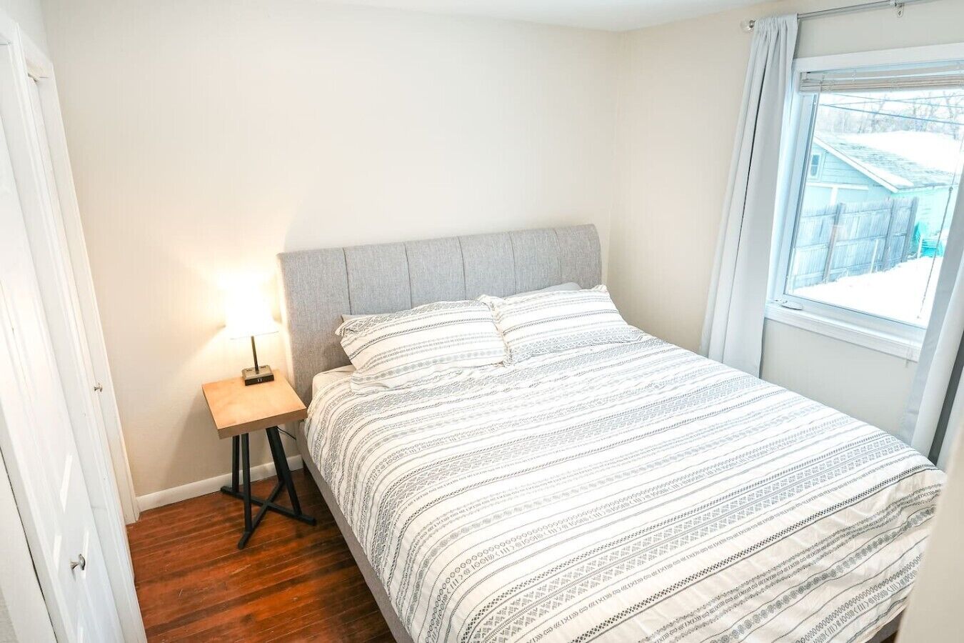 Ein Schlafzimmer mit Bett, Nachttisch, Lampe und Fenster.