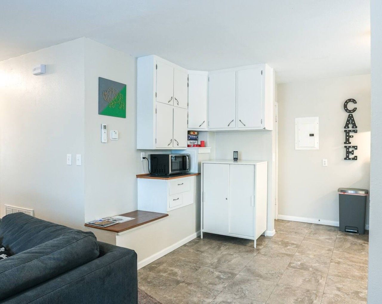 A compact living space with a kitchenette, a microwave, a cabinet, and a trash bin.