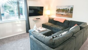 A living room with a grey sofa, a flat-screen TV, a lamp, and a painting on the wall.