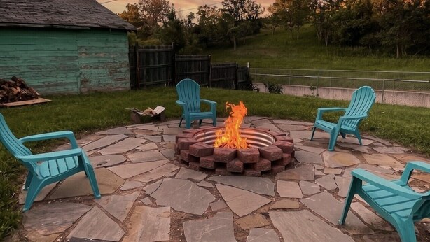 A stone patio with a fire pit and four turquoise chairs.