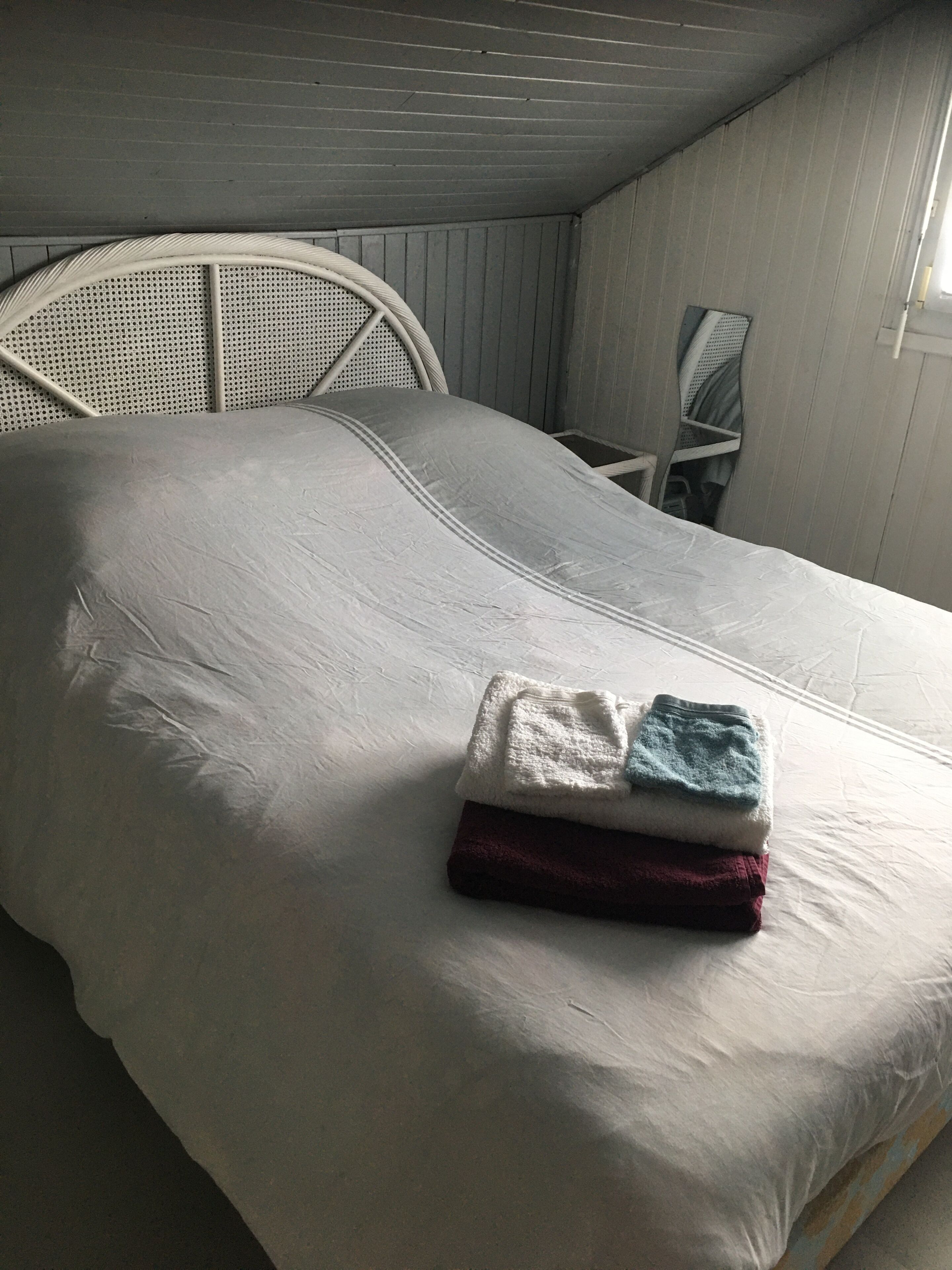 A bed with a white mattress and a headboard with a woven design. There are folded towels in white, blue, and maroon on the bed.