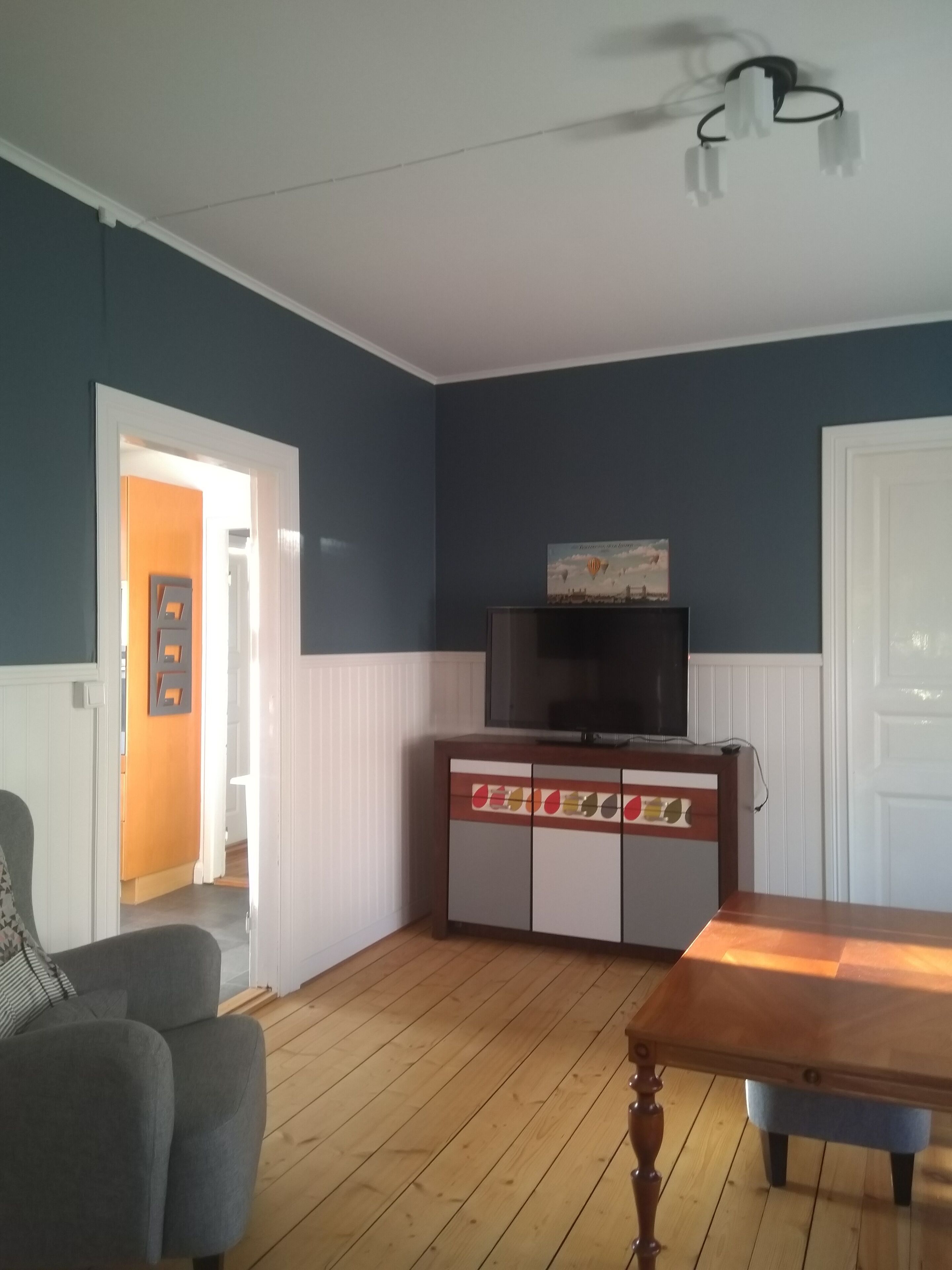 Un salon avec un plancher en bois, un téléviseur posé sur un meuble et une porte donnant sur une autre pièce.