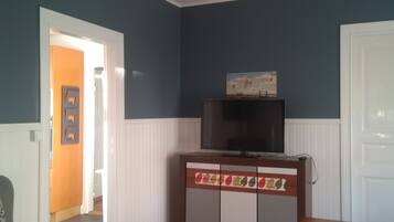 Un salon avec un plancher en bois, un téléviseur posé sur un meuble et une porte donnant sur une autre pièce.