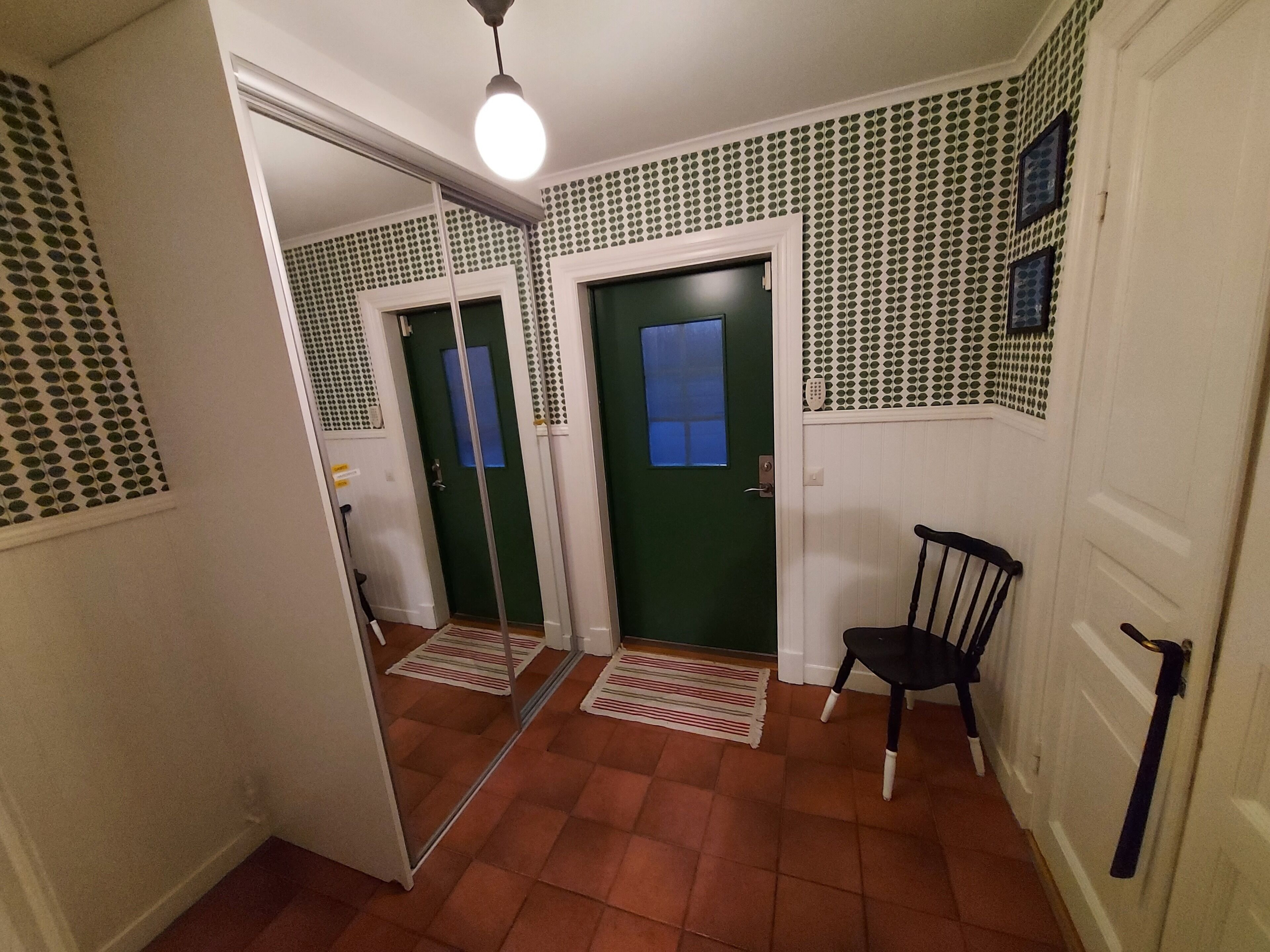 A hallway with a green door, a chair, and a patterned wall.