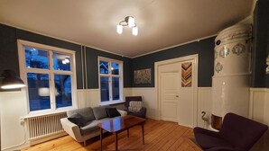 Une pièce avec un plancher en bois, un canapé, une table, une chaise violette et un radiateur.