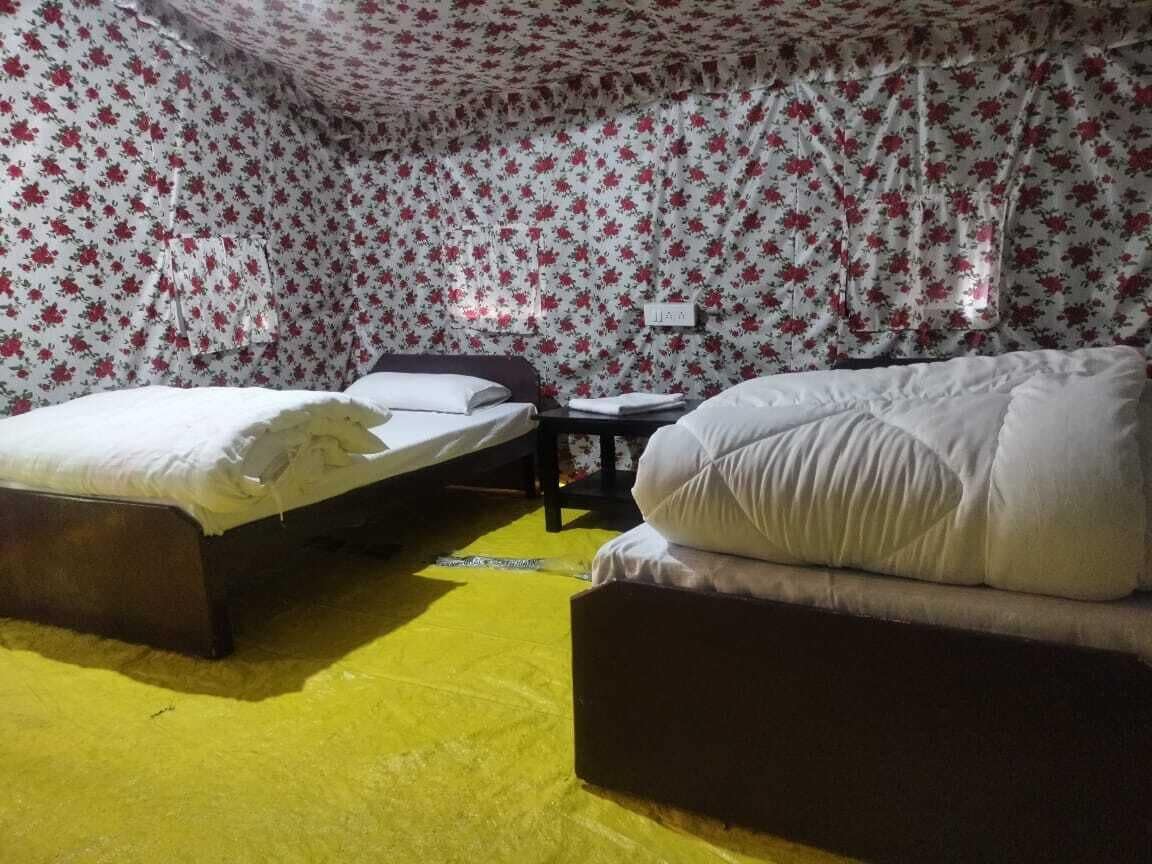 A room with two beds, a small table, and a wall with floral wallpaper.
