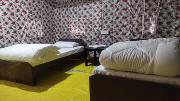 A room with two beds, a small table, and a wall with floral wallpaper.