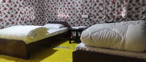 A room with two beds, a small table, and a wall with floral wallpaper.